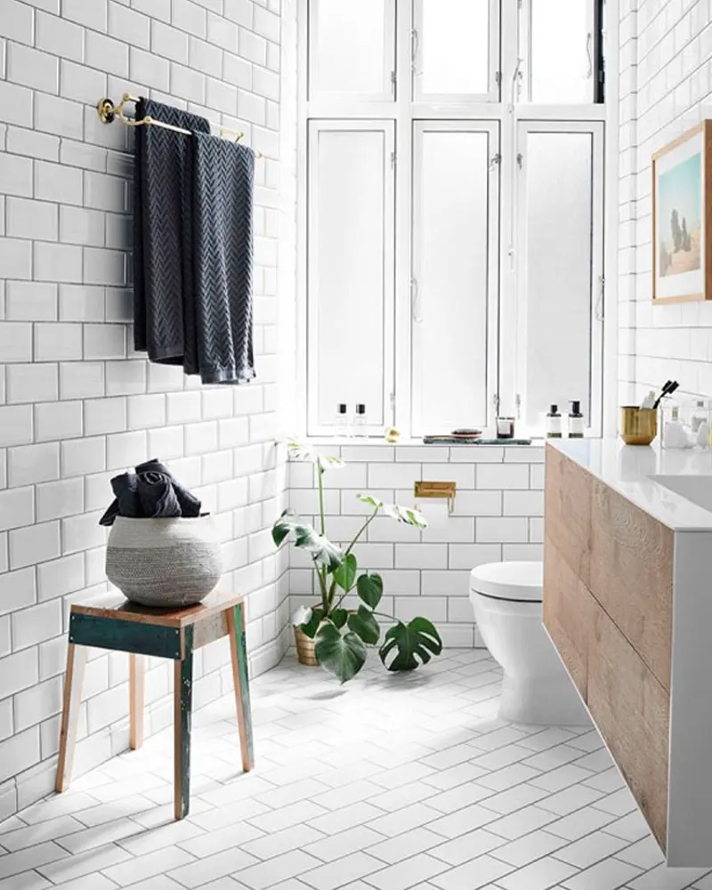 White subway tile bathroom with tall windows, wood stool, floating wood cabinet and plants