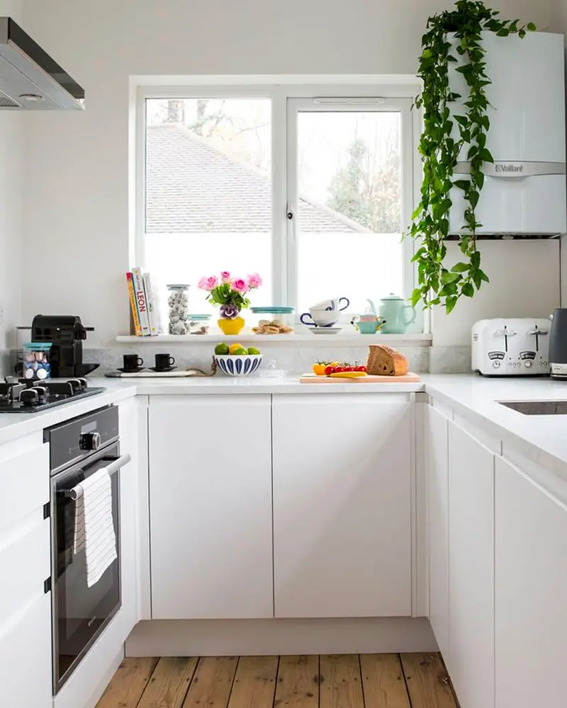 White U-shaped kitchen with handleless cabinets, trailing plant by the window and colorful dishes