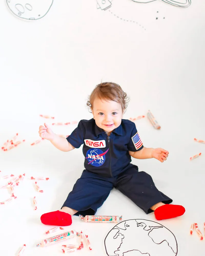 Toddler in a navy NASA jumpsuit with red socks sitting on the floor with a drawn globe