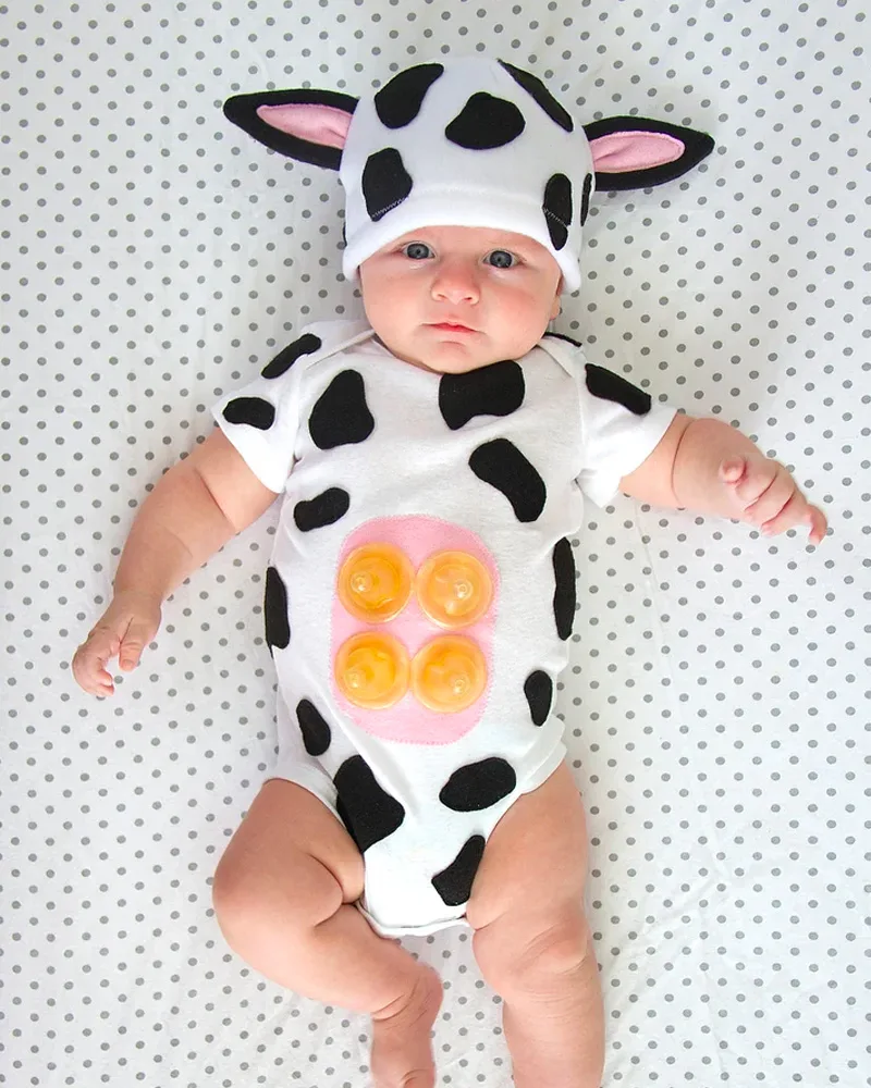 Baby in a white onesie with black felt spots, pink udder and a cow-eared hat