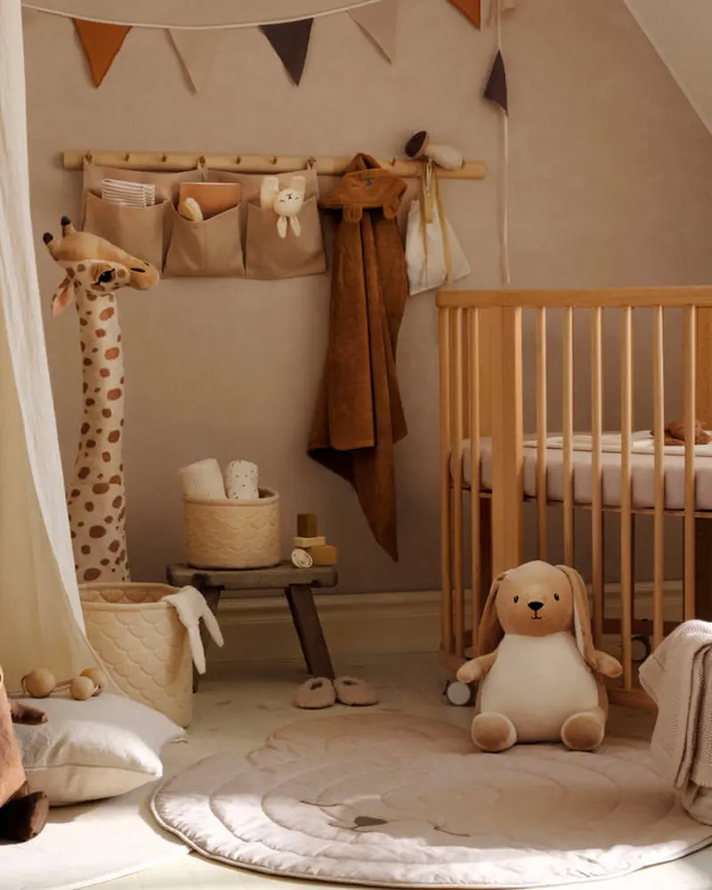 Beige nursery with wooden crib, wall pocket organizer, plush giraffe and bunny and pennant bunting