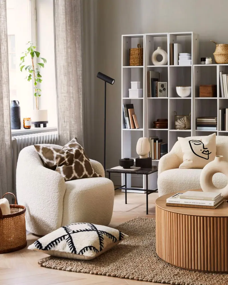 Small living room with cream boucle armchairs, a white cube bookcase, a fluted wood coffee table and a patterned pillow