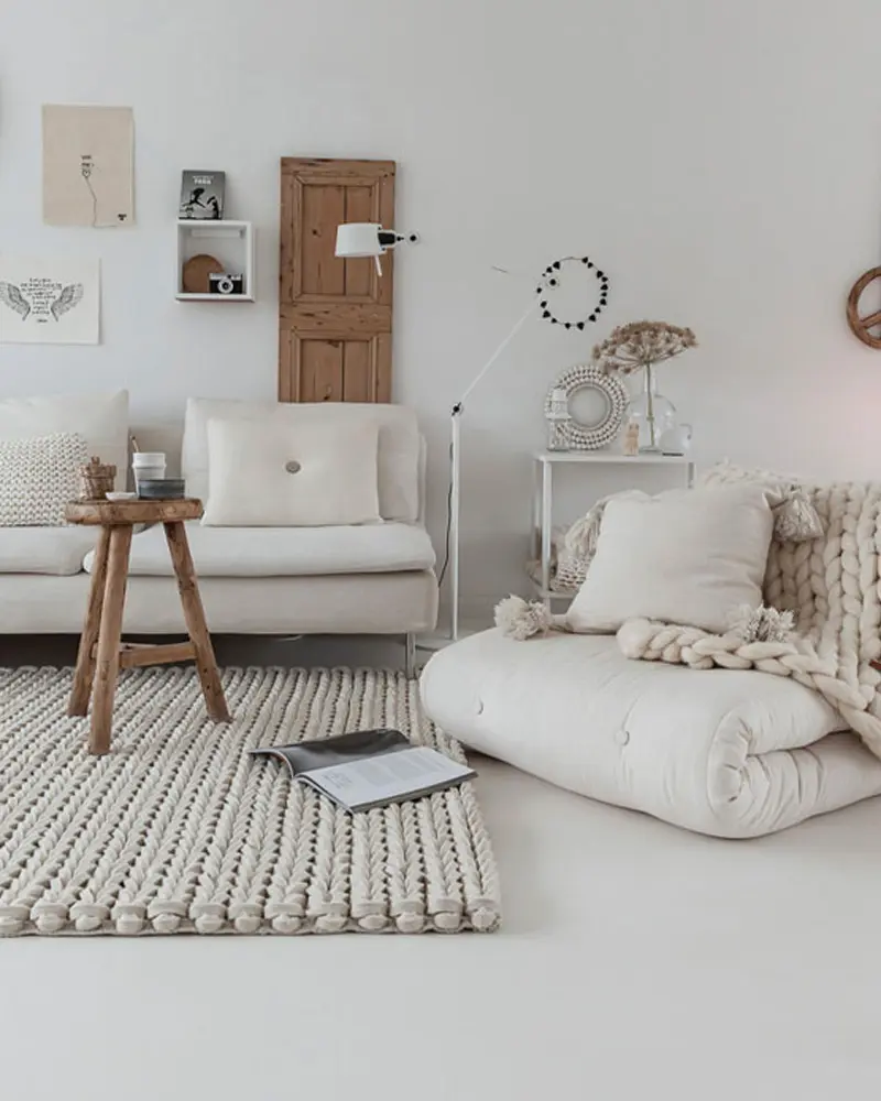 Cozy corner with a white sofa, a rolled floor futon with a chunky knit throw, a cable-knit rug and a wooden stool