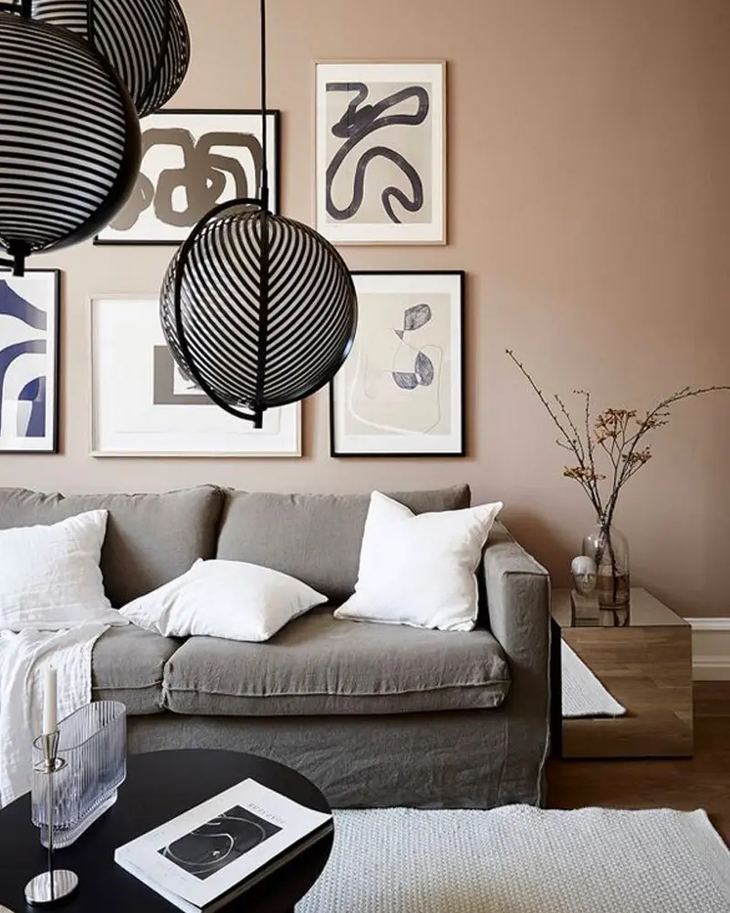 Living room with pinkish beige walls, a gray sofa with white pillows, black and white graphic art and black wire pendants