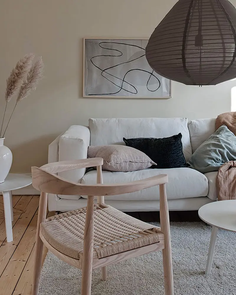 Japandi-style living room with beige walls, a white sofa, a dark paper lantern pendant, a light wood chair and line art