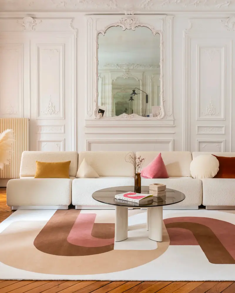 Elegant living room with white molded paneling, an ornate mirror, a cream modular sofa and a rug with pink and brown curves