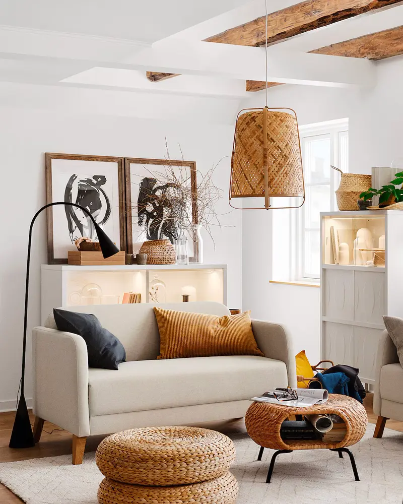 Living room with a cream loveseat, a woven rattan pendant, a rattan coffee table, stacked rattan poufs and framed art on a low cabinet