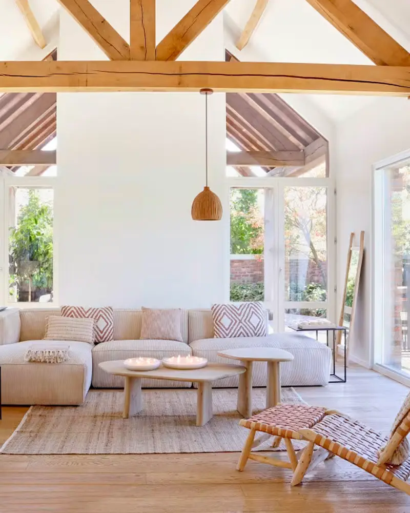 Bright living room with exposed wood trusses, a cream modular sofa with patterned pillows, round wood coffee tables and a jute rug