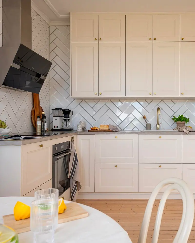 Cream shaker cabinets with white herringbone tile backsplash and round marble table with lemons