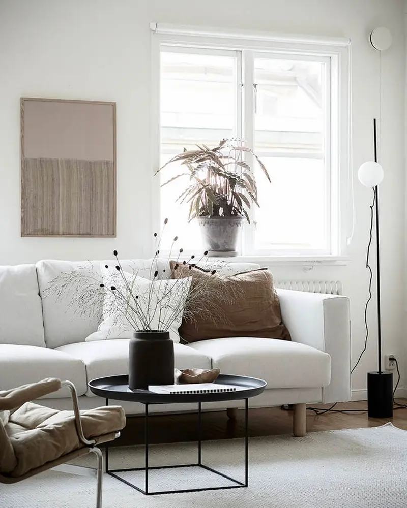White sofa with taupe pillows, black wire coffee table and a framed textile art piece