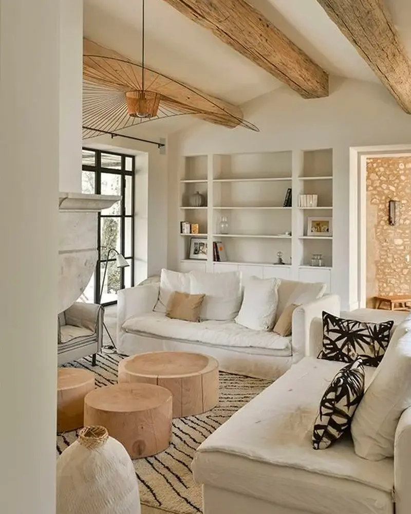 White sofas with graphic pillows, wood stump tables, exposed beams and built-in shelves