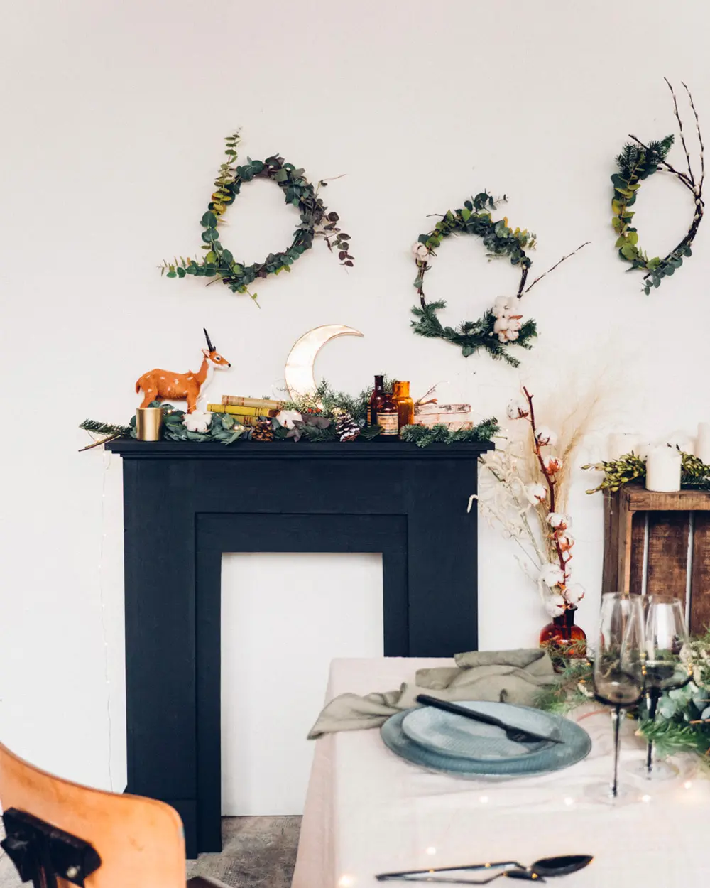 Black faux fireplace frame with greenery and a deer figurine on the mantel and three wreaths above