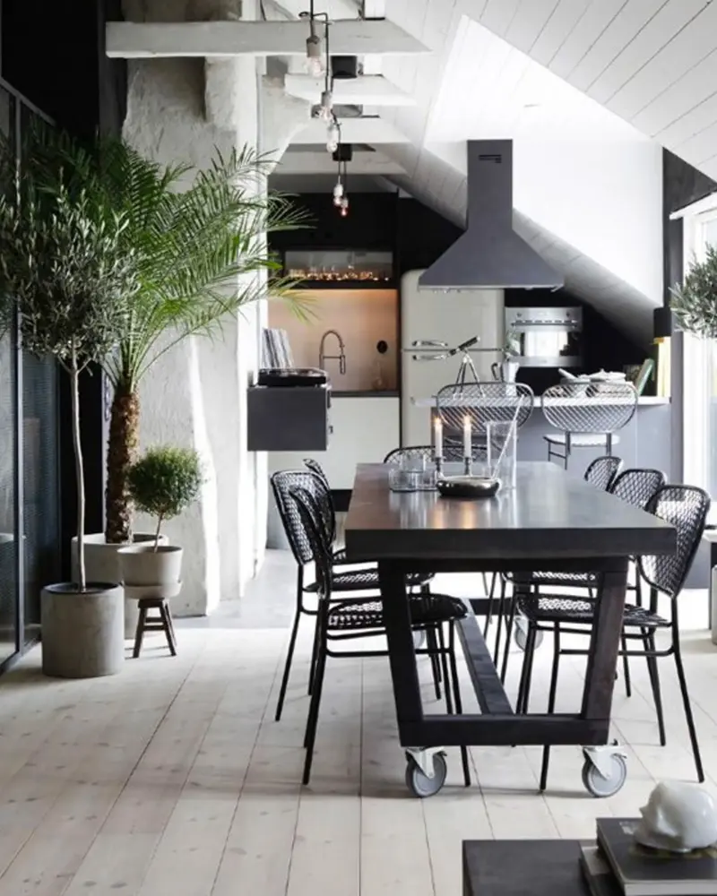 Black steel dining table on casters with black wire chairs and potted palms