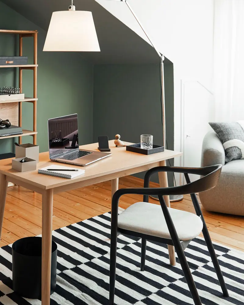 Wood desk with black bentwood chair, white floor lamp, sage green wall and black and white striped rug