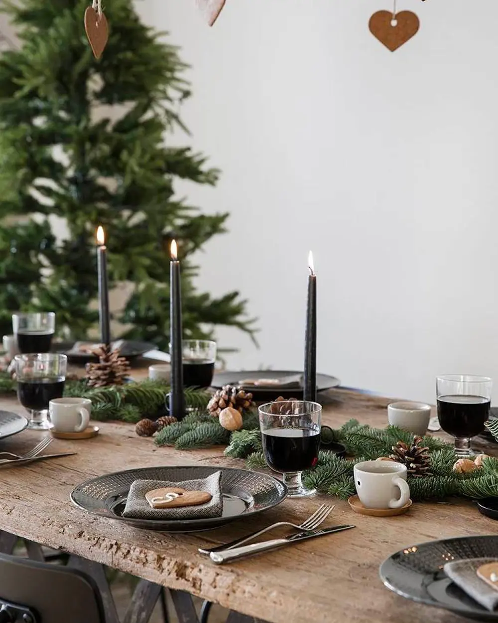 Rustic wood table with black taper candles, fir garland, pinecones and dark glasses of mulled wine