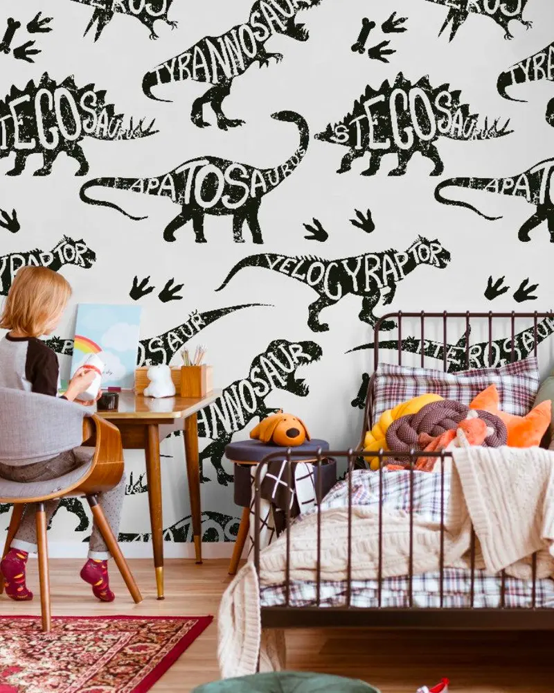 Kids room with black and white dinosaur name wallpaper, iron bed and child drawing at a desk