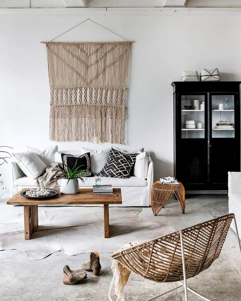 White sofa with black and white pillows, large macramé wall hanging, wood coffee table and black cabinet