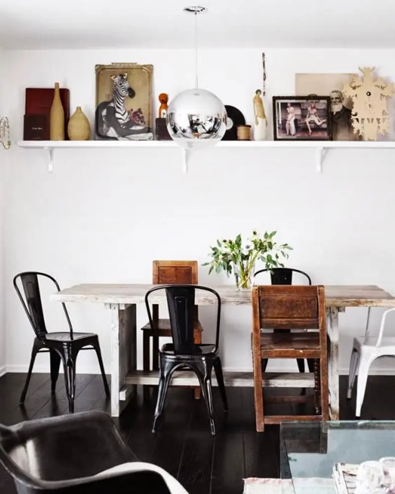 White dining table with black metal chairs, a rustic wood chair and a display shelf