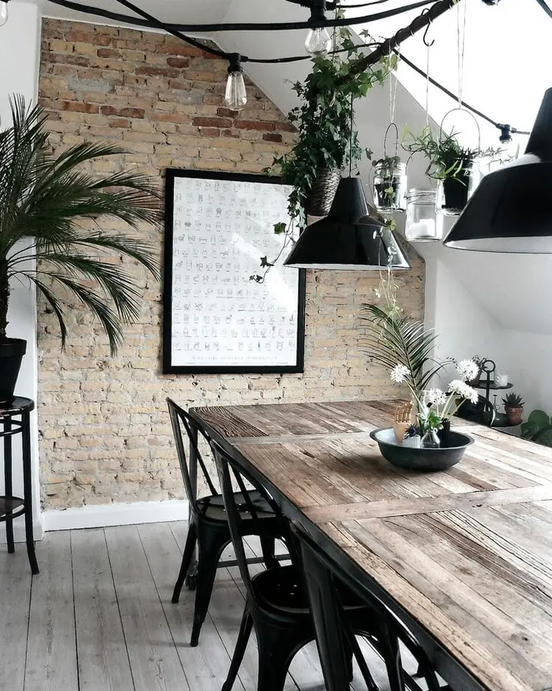 Rustic plank table with black metal chairs, a brick wall, black pendants and hanging plants