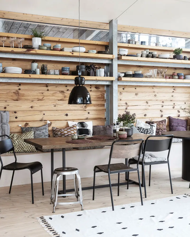 Wood plank wall with open shelves, banquette with pillows, black chairs and metal stool