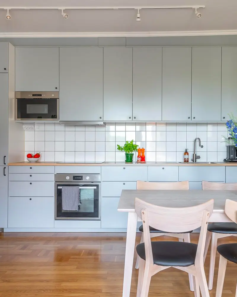 Pale blue cabinets with white square tile, wood counter, gray table and white wood chairs