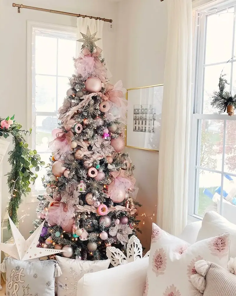 Christmas tree decorated with blush pink and white ornaments and paper stars beside a white sofa