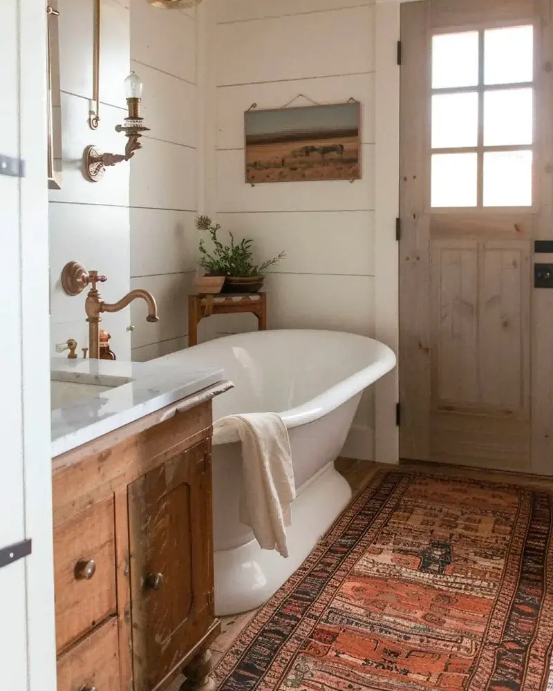 White rolltop tub on a red and orange kilim runner with brass fixtures, a wood vanity and a glass-paned door