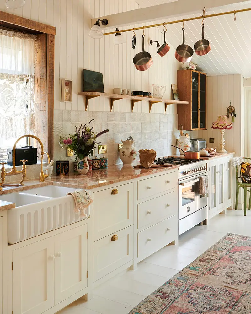 Cream cabinets, a fluted apron sink, copper pans on a brass rail and a faded vintage rug