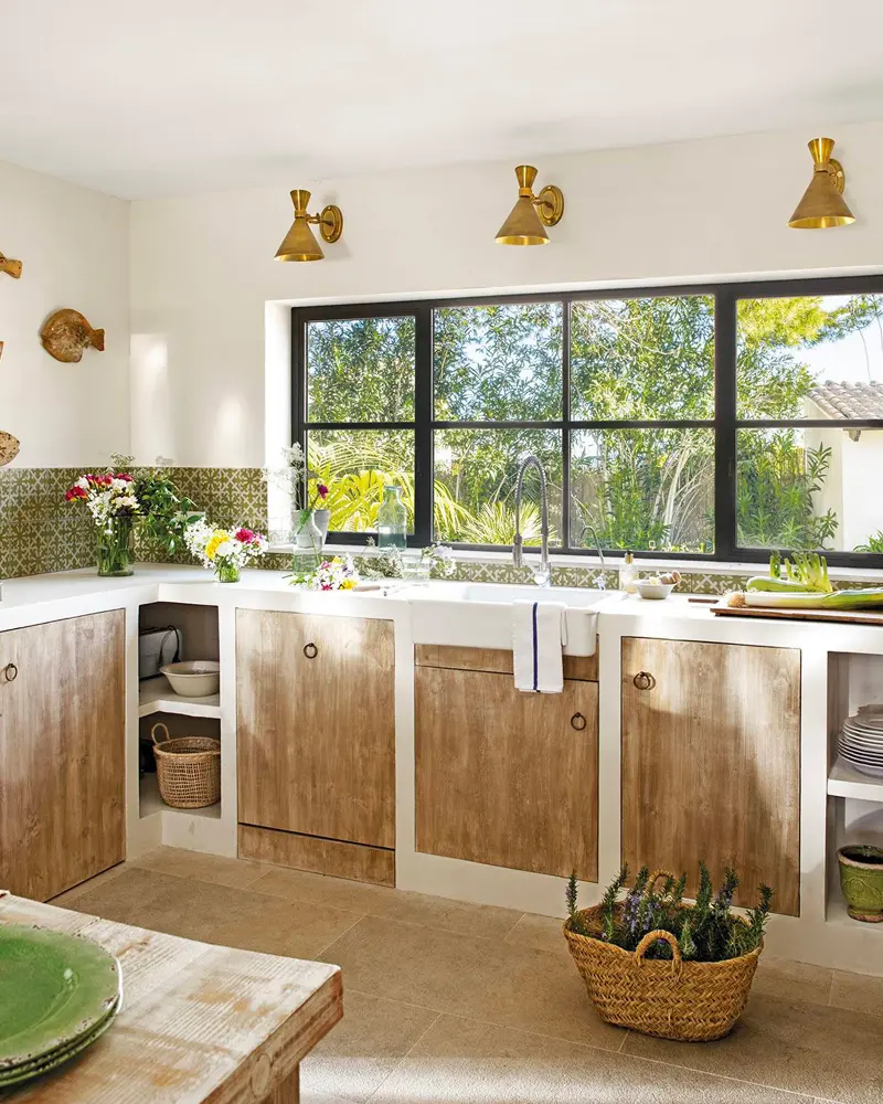 White built-in counters with weathered wood doors, brass sconces and a large black-framed window