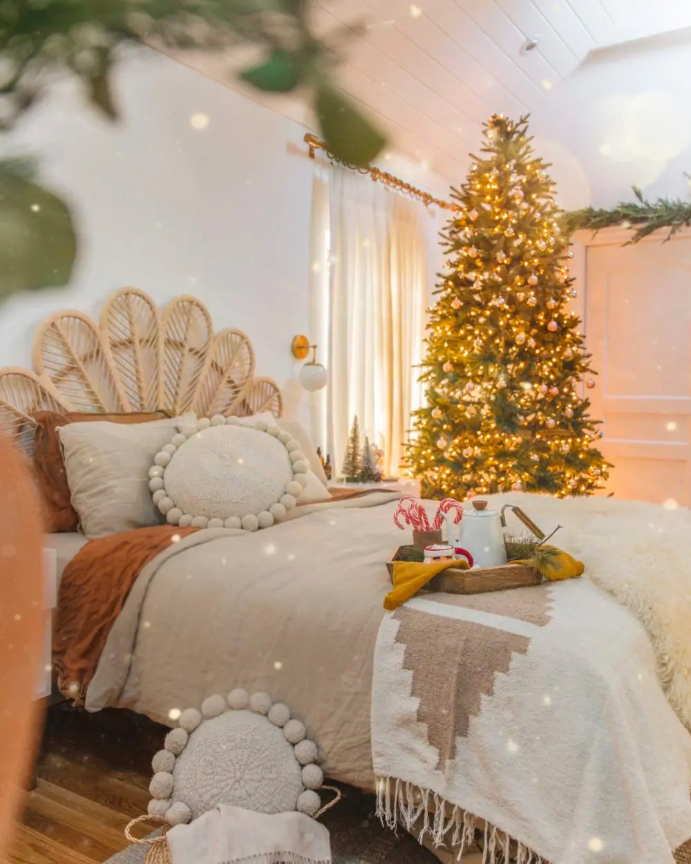 Boho bedroom with rattan headboard, pompom pillows and a glowing Christmas tree by the window