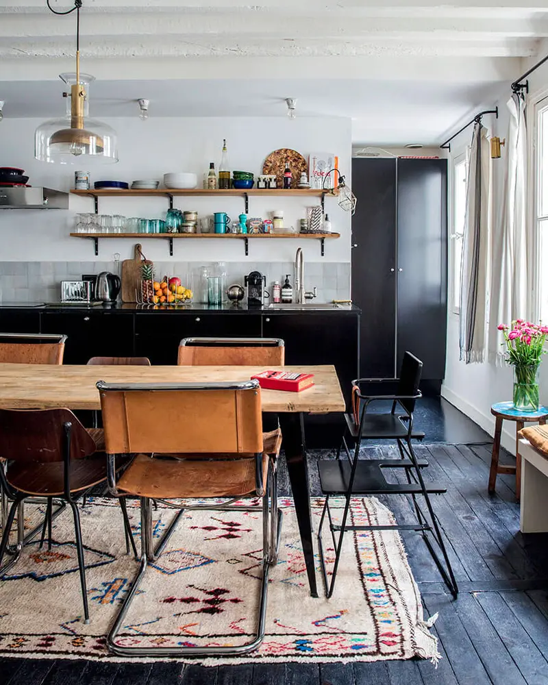 Wood dining table with cognac leather sling chairs, a Berber rug and open kitchen shelves