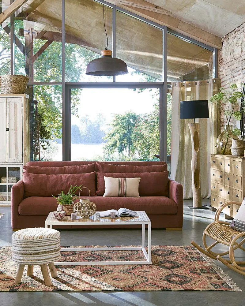 Rust velvet sofa, white metal coffee table, striped pouf and kilim rug under a glass roof