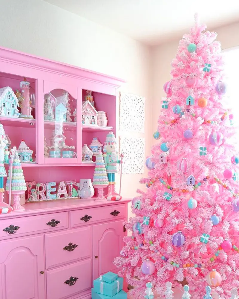 Bright pink Christmas tree with pastel ornaments next to a pink painted hutch filled with gingerbread houses