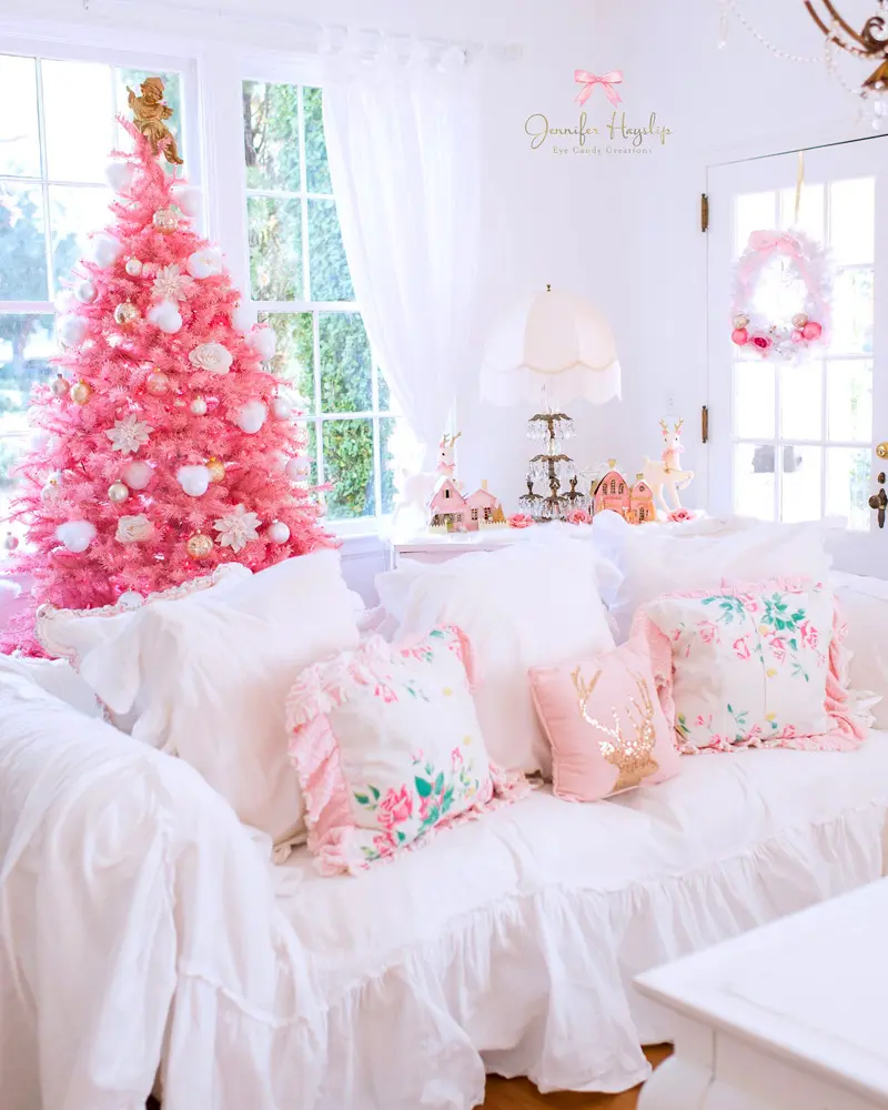 Bright pink Christmas tree in a white living room with a slipcovered sofa and floral pink pillows