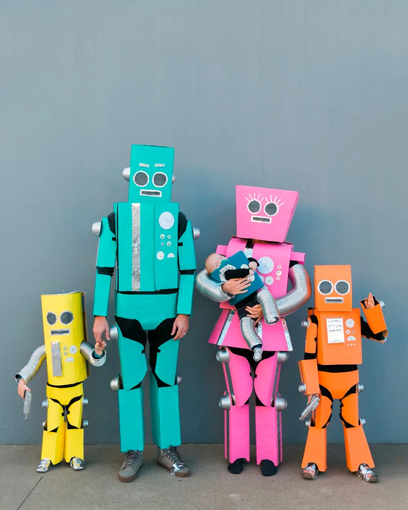 Family of four in colorful cardboard robot costumes in teal, pink, orange and yellow