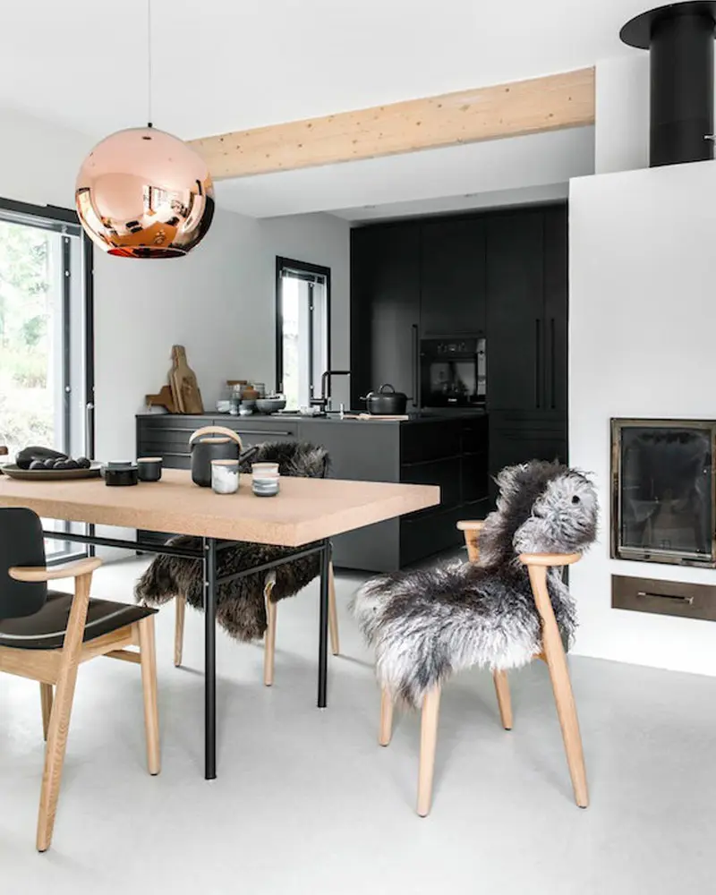 Light wood table with sheepskin-covered chairs, copper globe pendant and black kitchen behind