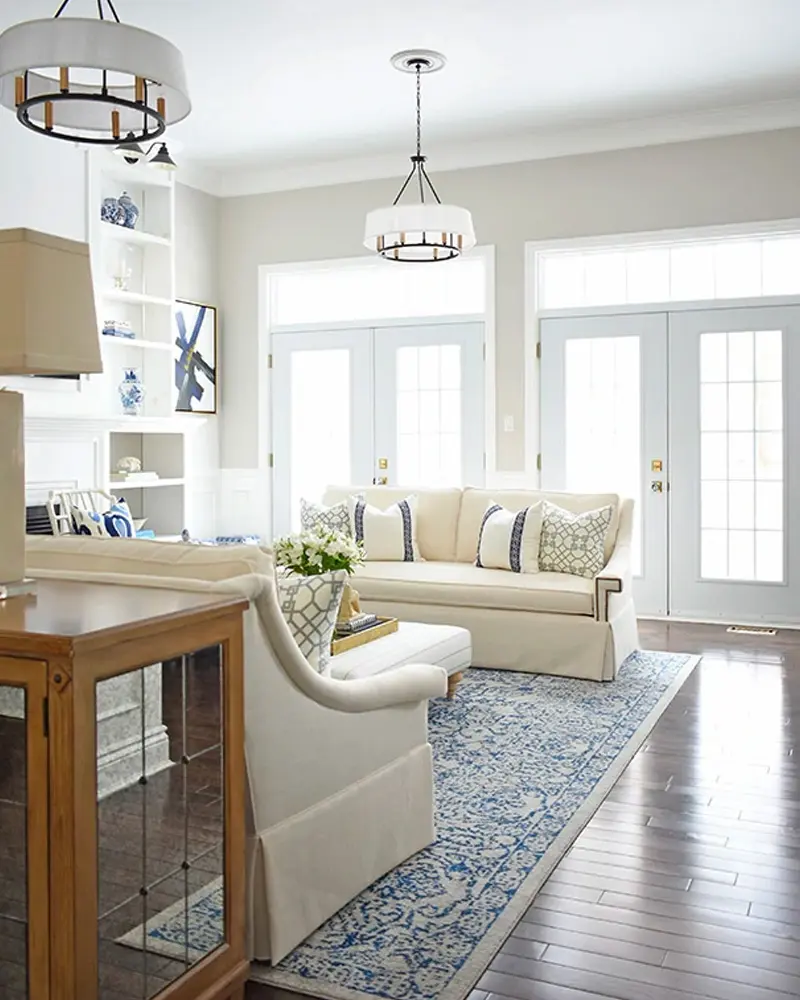 Bright living room with cream sofas, a blue and white patterned rug, a glass-front cabinet, a drum pendant and white French doors