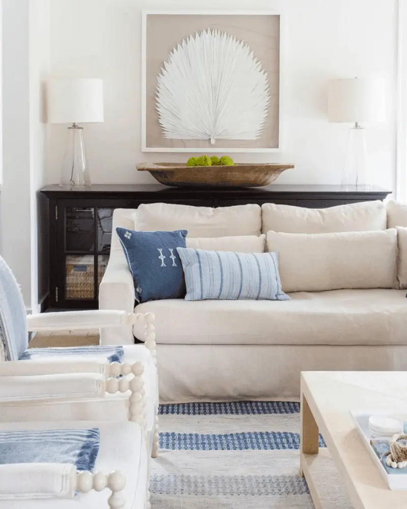 Coastal living room with a cream sofa, navy and blue striped pillows, a framed white sea fan, a dark console with white lamps and a blue striped rug