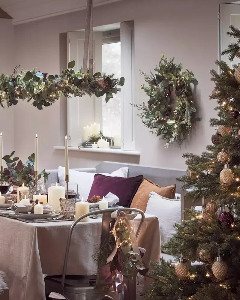 Dining room with hanging eucalyptus garland, wreath, plum cushions and lit tree