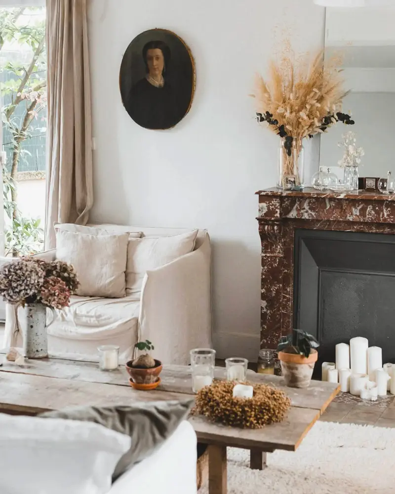 White linen sofa by a marble fireplace with candles, dried flowers and a vintage portrait
