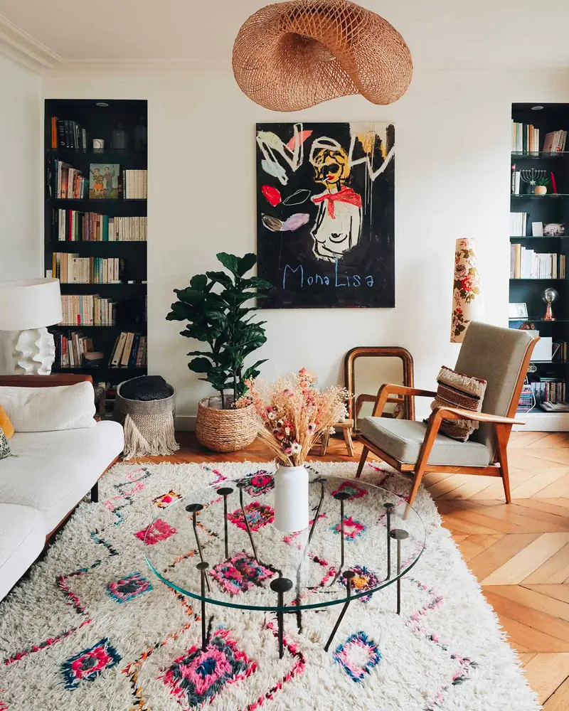 Glass coffee table on a colorful Berber rug, bold artwork, black bookcases and woven pendant