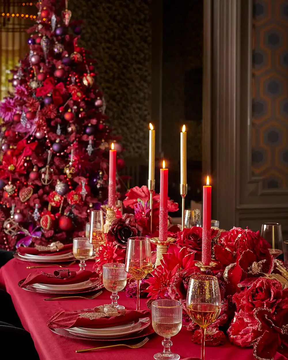 Moody dining table with red tablecloth, red taper candles and red flowers in front of a red tree