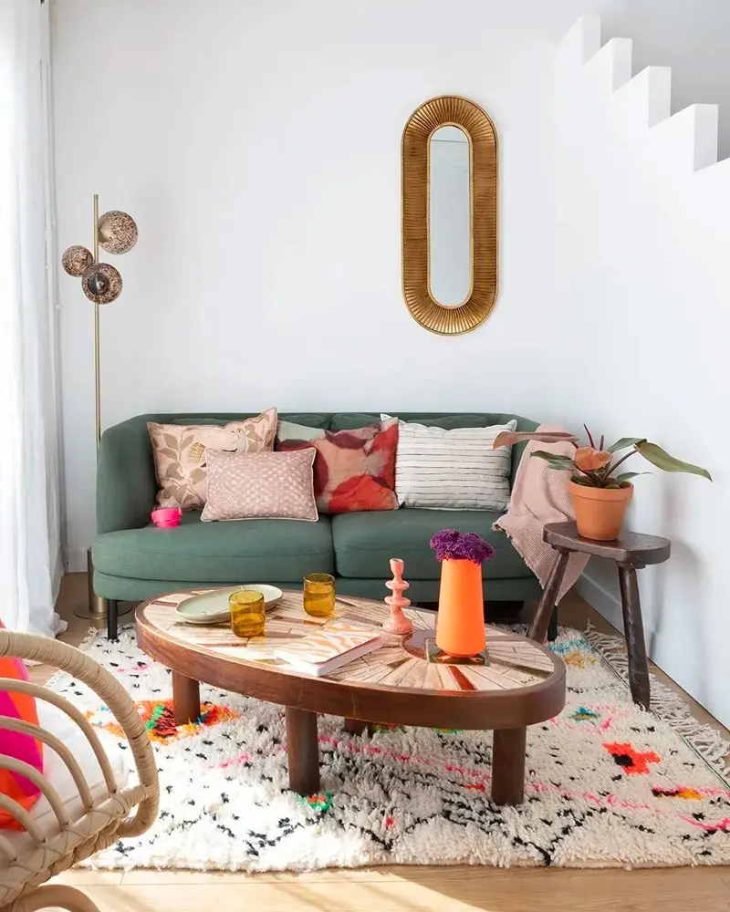 Green sofa with patterned pillows, oval wood coffee table, Berber rug and tall rattan mirror