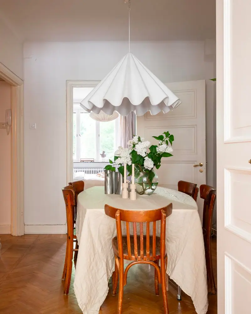 Pleated white pendant over a round table with linen cloth, bentwood chairs and white flowers