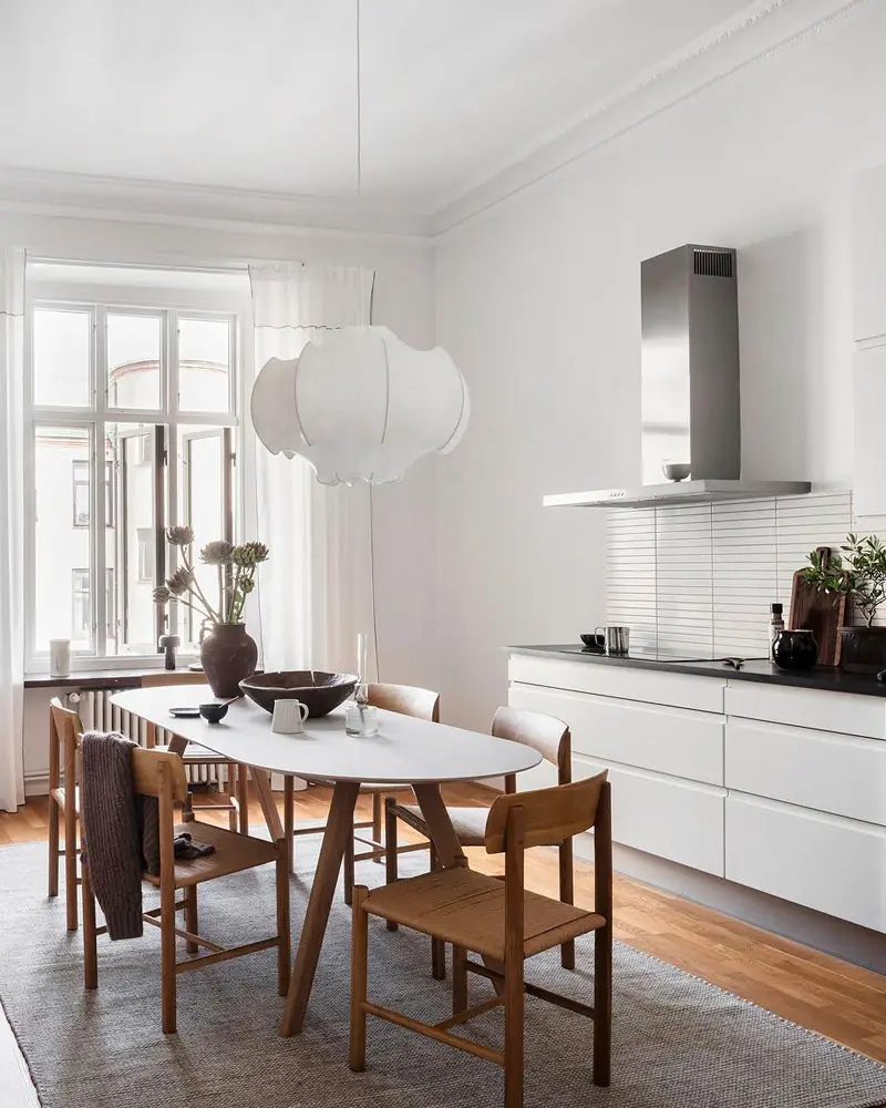 Bright white kitchen with stainless hood, oval dining table, wood chairs and white cloud pendant