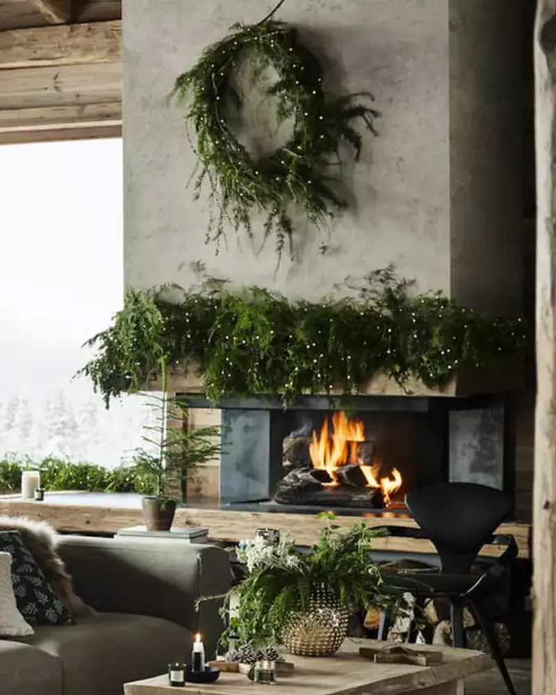 Modern concrete fireplace with a loose wreath and a thick fresh greenery garland above a lit fire