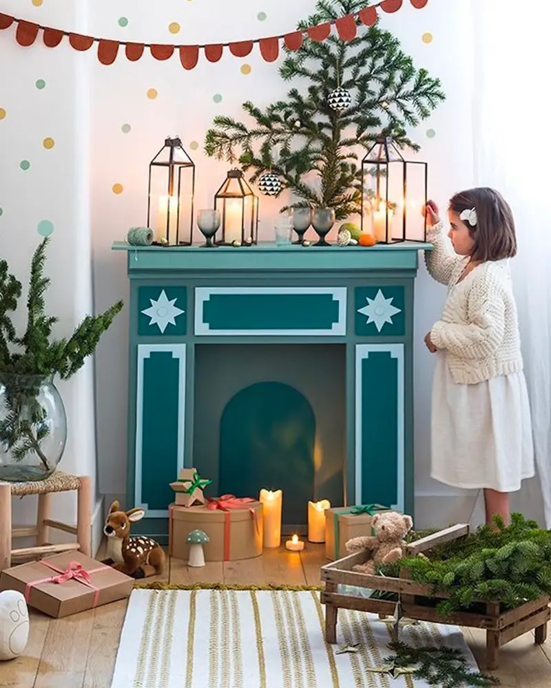 Teal painted faux fireplace with lanterns and candles, a fir branch and a little girl reaching up