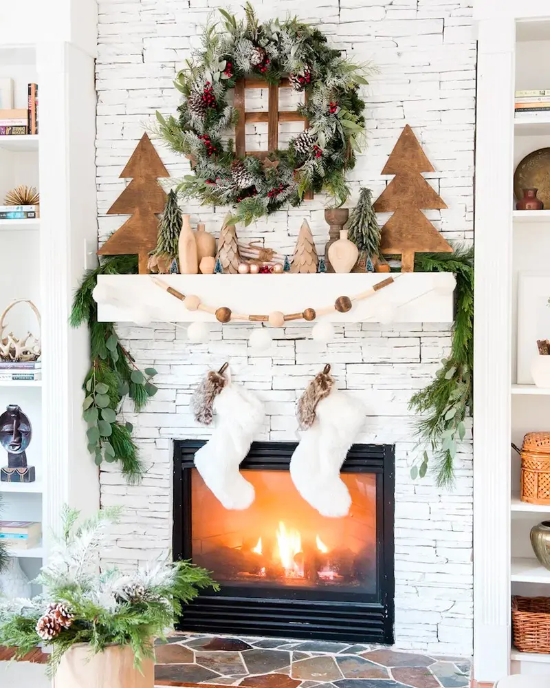 White brick fireplace with a pine cone wreath, cutout wood trees, a wood bead garland and white stockings