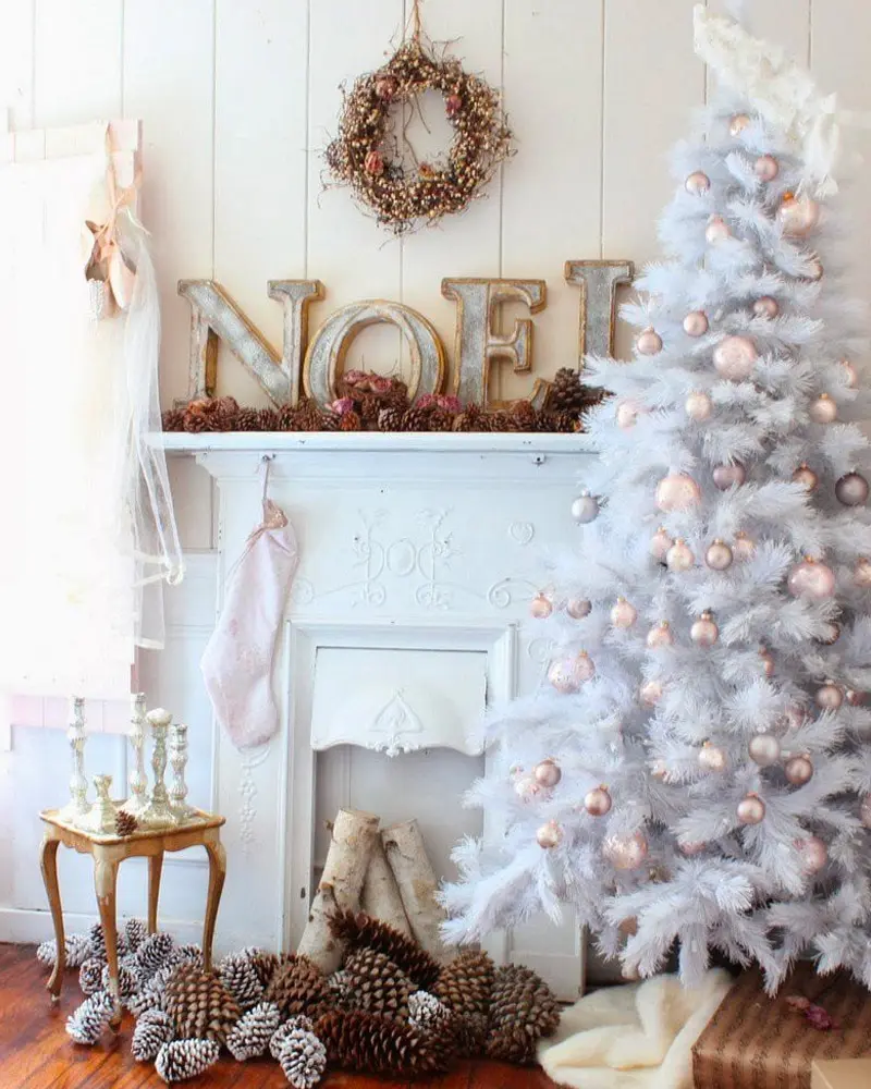 White mantel with metal NOEL letters, a pine cone wreath, a white tree with blush ornaments and pine cones