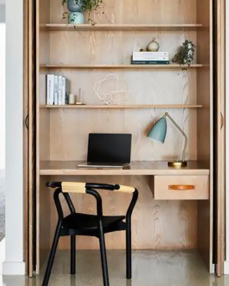 Plywood-lined closet office with laptop, blue lamp and black chair